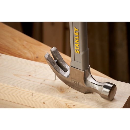 STANLEY STHT0-51309 claw hammer, silver and grey, driving nail into wooden beam, close-up photo.