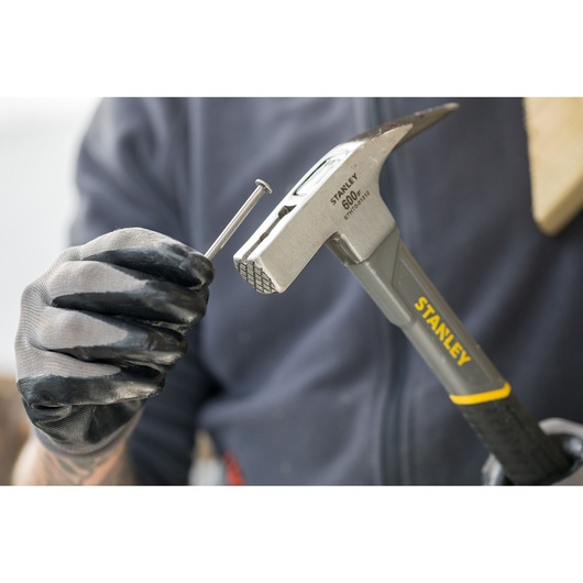 Stanley STHT0-51312 hammer held with gloved hand, positioning a nail, close-up photo.