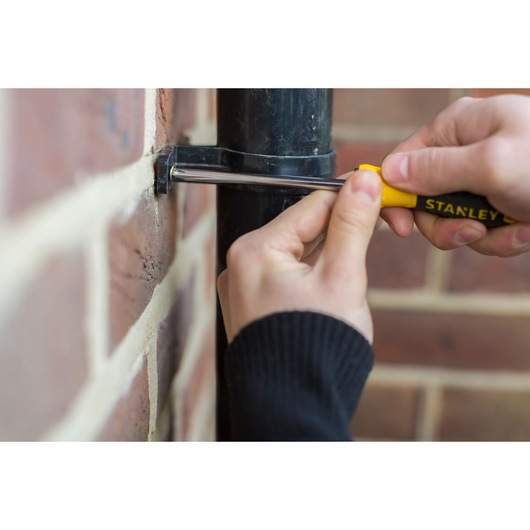 STANLEY STHT0-60273 screwdriver used to tighten a screw on a pipe bracket mounted on a brick wall.