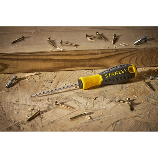 STANLEY STHT0-60358 flathead screwdriver with yellow and black handle on wooden surface with scattered screws.