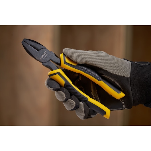 Stanley STHT0-74456 combination pliers held in gloved hand, yellow and black handle, close-up photo.