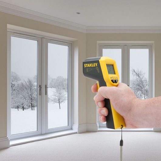Stanley STHT0-77365 infrared thermometer held in hand, measuring window temperature indoors.