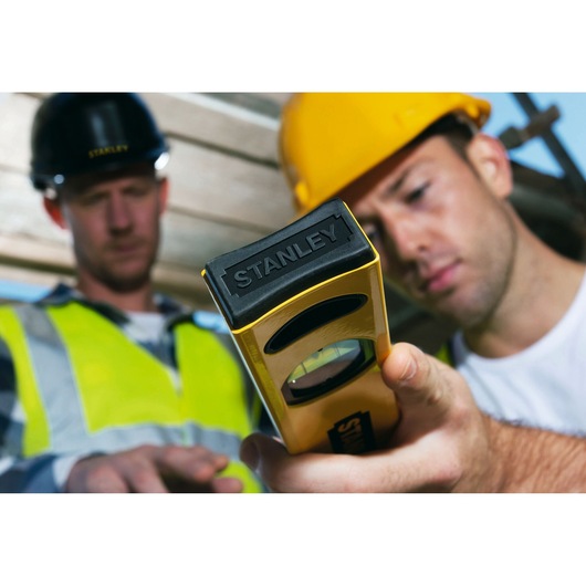 Photo of STANLEY STHT1-43102 level tool in use at construction site, close-up on yellow and black tool.