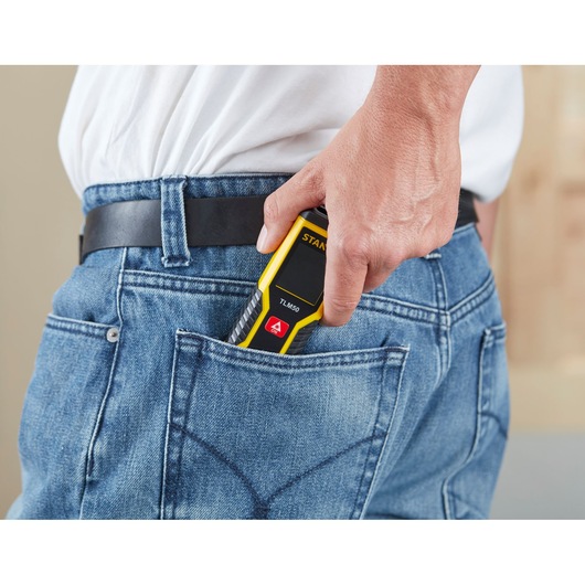 STANLEY STHT1-77409 laser distance measurer in a person's hand, being placed into a jeans back pocket.