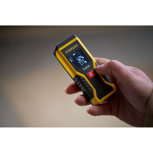 Photo of STANLEY STHT1-77409 laser distance measurer held in hand, yellow and black with digital display.