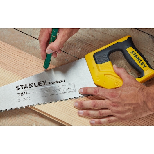 STANLEY STHT20348-1 hand saw with yellow handle on wood, close-up showing cutting teeth and brand details.