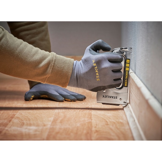 STANLEY STHT6-70410 multi-tacker used on floor trim, close-up angle, gloves visible.