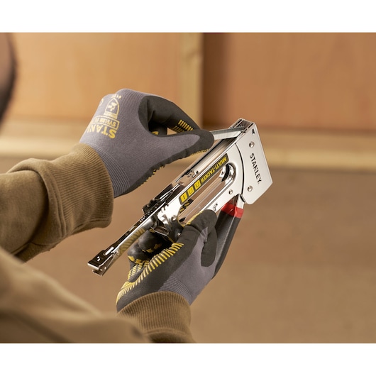 Photo of STANLEY STHT6-70410 multi-tacker stapler in use, held by gloved hands indoors.