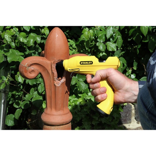 Stanley STHT6-70416 yellow glue gun for repairing outdoor terracotta ornament, held by hand.