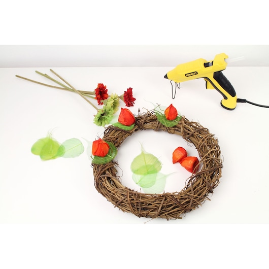 STANLEY STHT6-70417 yellow glue gun, floral stems, and vine wreath with red flowers on white background, top view.