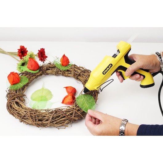 STANLEY STHT6-70417 yellow hot glue gun being used to attach leaves to a decorative wreath.