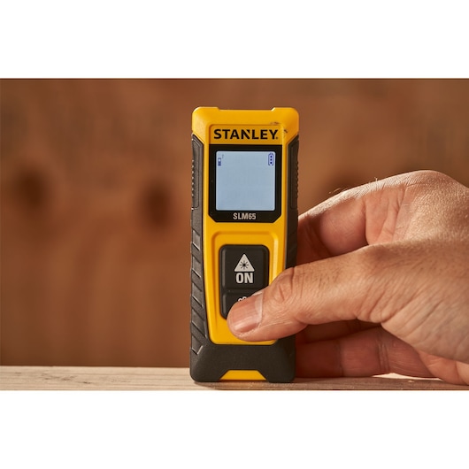 Photo of STANLEY STHT77065-0 laser distance measurer held by hand, yellow and black, close-up view.