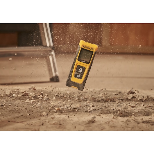 STANLEY STHT77065-0 laser distance measurer in yellow and black, dropping onto a dusty floor.