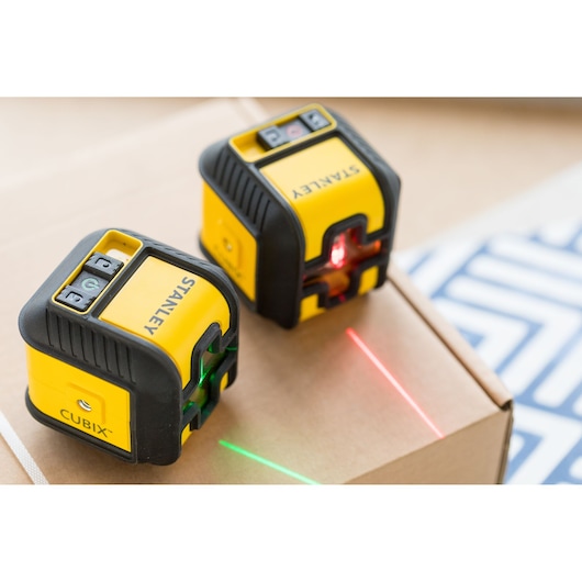 STANLEY STHT77499-1 laser levels in yellow and black projecting red and green lines on a cardboard box.