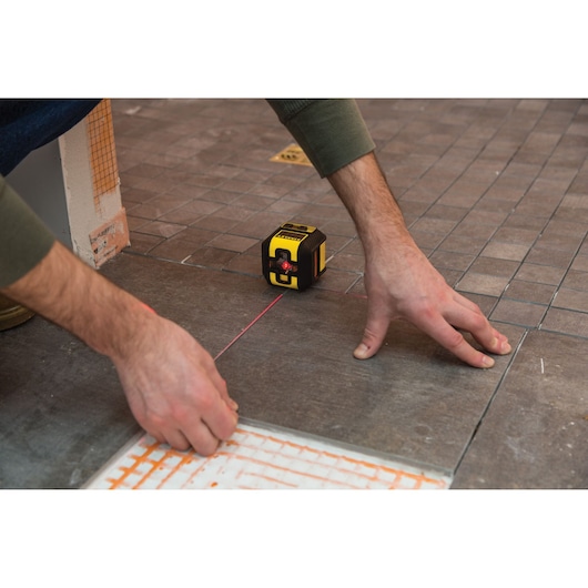 STANLEY STHT77502-1 laser level used for precise tile alignment on a brown tiled floor.