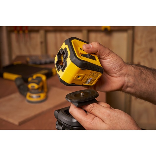 STANLEY STHT77611-0 laser level being mounted on a tripod base in a workshop setting.
