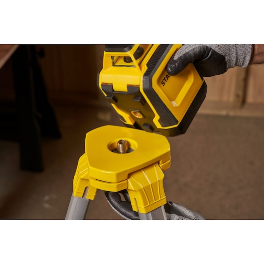 STANLEY STHT77616-0 photography of yellow laser level being mounted on tripod, close-up view.
