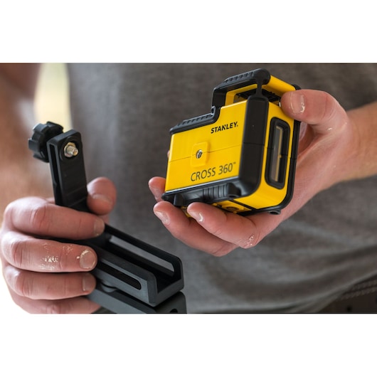 STANLEY STHT77640-1 yellow CROSS 360° laser level held in hand, with mounting bracket visible.