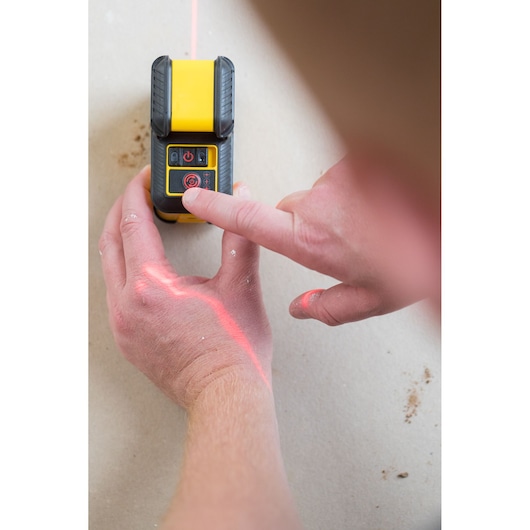 STANLEY STHT77640-1 laser level in use, hand pressing button with red laser line on surface.
