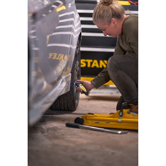 STANLEY STHT80874-0 digital tire pressure gauge used on car tire, close-up, tool in hand, yellow and black.