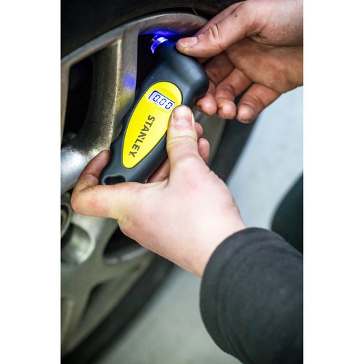 STANLEY STHT80874-0 digital tire pressure gauge, handheld, used on car wheel, close-up photography.