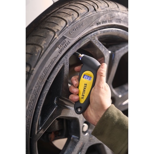 STANLEY STHT80874-0 digital tire pressure gauge displaying reading, shown in use on a car tire close-up.