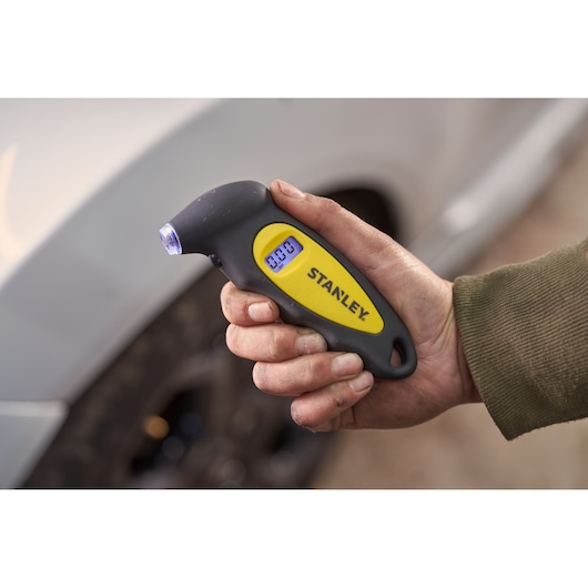 Photo of STANLEY STHT80874-0 digital tire pressure gauge held in hand near a car tire.