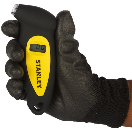 Stanley STHT80874-0 digital tire gauge in black and yellow, held in a gloved hand, front angle.