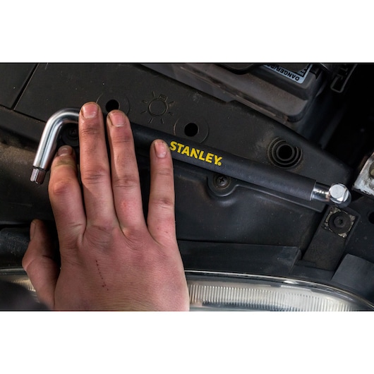 Photo of STANLEY STHT80879-0 L-shaped tool held by hand, shown in automotive engine context.