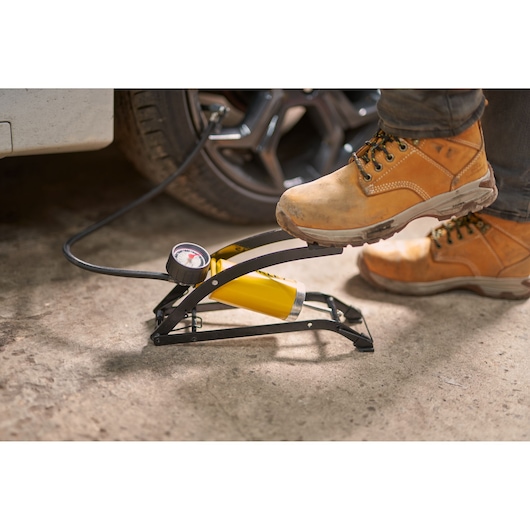 STANLEY STHT80894-1 foot-operated air pump with gauge inflating car tire, close-up in workshop.
