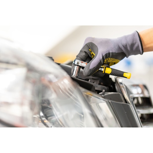 STANLEY STMT82663-0 ratchet used on car headlight, close-up showing grip and tool details.