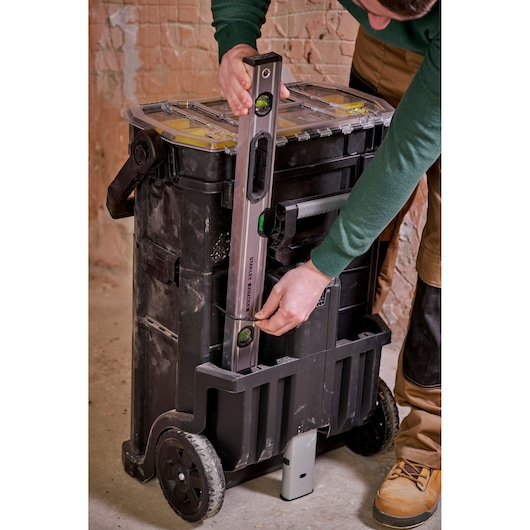 STANLEY STST1-79231 photography of black wheeled tool box with level being secured, front angle.