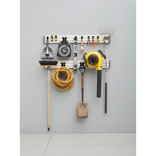 STANLEY STST22000-1 wall-mounted organizer rail holding various tools including rake, blower, broom, cord, and hand tools.