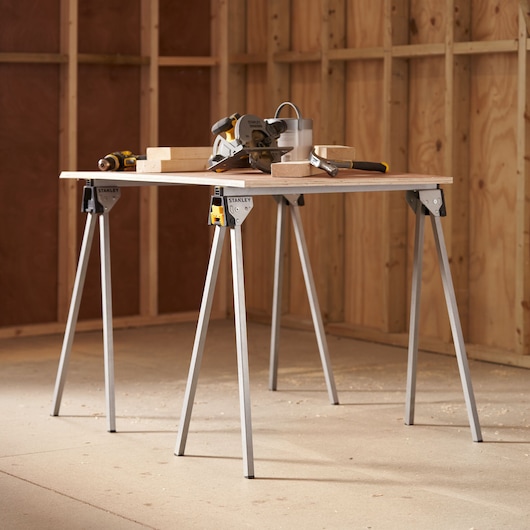 STANLEY STST81337-1 folding sawhorse table in workshop with tools and wood blocks on top.
