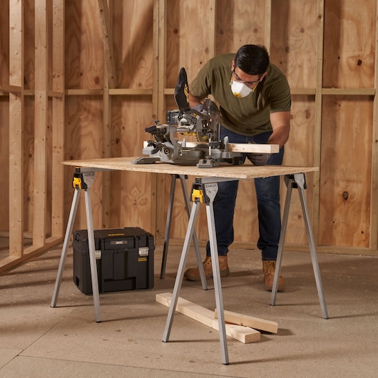 STANLEY STST81337-1 metal sawhorse pair supporting wood board in workshop, man working, tool box nearby.