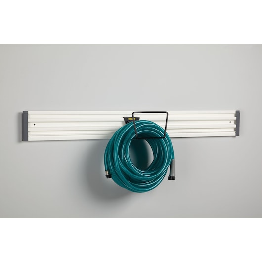 STANLEY STST82604-1 wall-mounted white rail with hook holding a coiled green hose, front angle.